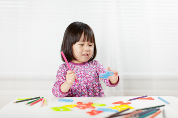 toddler girl practice writing letters on white paper against white background