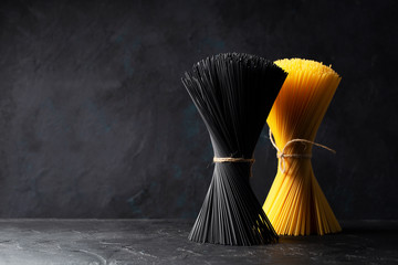 Dry black pasta with cuttlefish ink and yellow spaghetti stands on black background. Space for text.