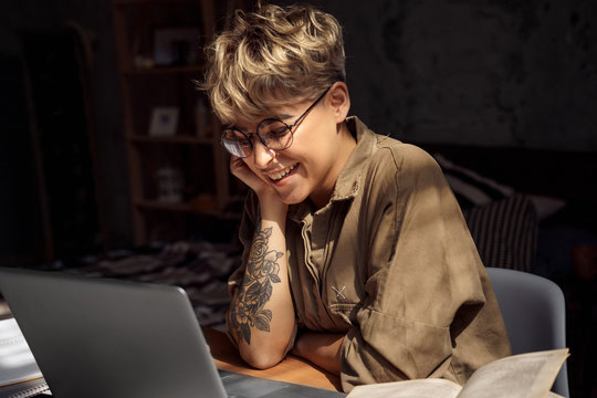 Distance Education. Young woman short hair in glasses sitting at desk studying online on laptop looking at screen laughing cheerful