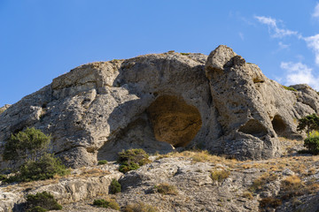 Beautiful view of big mountain with grotto Aeolian Harp on trail Alchak-Kaya. Alchak Cape in south coast of resort Sudak city, Crimea, Russia.