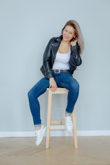 Blonde woman in leather jacket near grey wall. Minimalistic apartment.