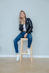 Blonde woman in leather jacket near grey wall. Minimalistic apartment.