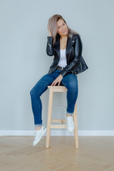Blonde woman in leather jacket near grey wall. Minimalistic apartment.