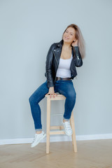 Blonde woman in leather jacket near grey wall. Minimalistic apartment.
