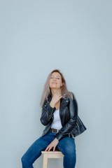 Blonde woman in leather jacket near grey wall. Minimalistic apartment.