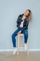 Blonde woman in leather jacket near grey wall. Minimalistic apartment.