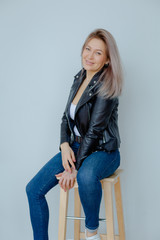 Blonde woman in leather jacket near grey wall. Minimalistic apartment.