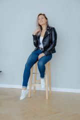 Blonde woman in leather jacket near grey wall. Minimalistic apartment.