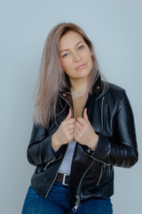 Blonde woman in leather jacket near grey wall. Minimalistic apartment.