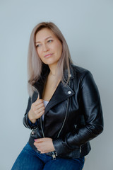 Blonde woman in leather jacket near grey wall. Minimalistic apartment.