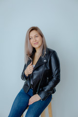 Blonde woman in leather jacket near grey wall. Minimalistic apartment.