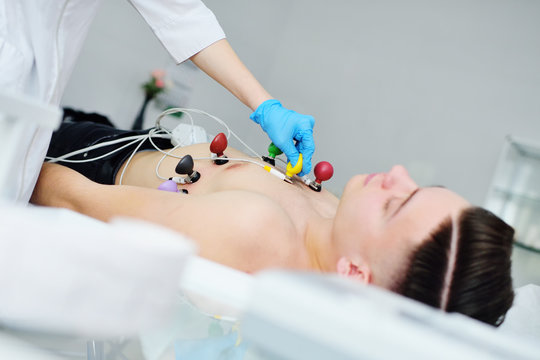 doctor of cardiology - a young pretty woman puts rubber vacuum electronic sensors for ECG or electrocardiogram on the body of a male patient. Prevention of cardiovascular diseases