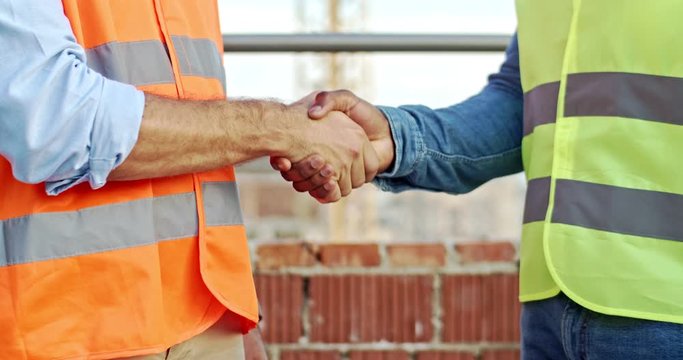 Close up of the African American and Caucasian male hands shaking at the constructing site. Two builders or foremen greeting. Outdoors.