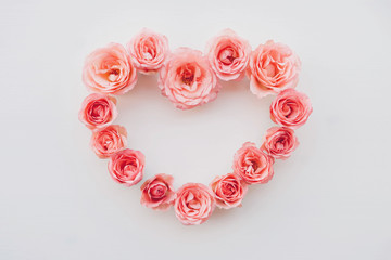 Obraz premium Heart frame of fresh pink roses in full bloom on white background. Bunch of flowers.