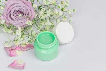 Green cosmetic jar with cleansing balm (oil) on a white background with flowers roses and petals, mockup, beauty product and spa concept, close up, copy space