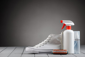 White canvas sneaker and footwear care supplies on gray background