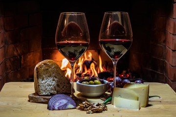 Two glasses of wine, cheese, bread and fruit on fire background