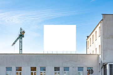Blank white advertising billboard on the roof of the building. There is construction crane in the background.
