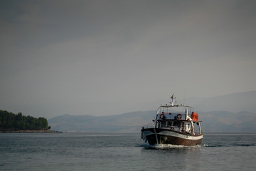 An older type of a middle sized boat or ship is naviganting on mediterranean sea close to the shore of Corfu island, Greece.