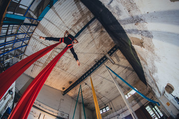 A woman aerial gymnastic dancer on silk rope performing in an industral environment of an abandoned...