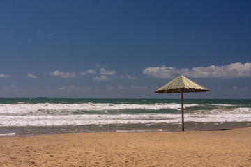 A single thatched umbrella on a sandy beach in Durban, South Africa with big ocean with waves in the background.