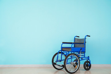 Fototapeta na wymiar Empty wheelchair near color wall