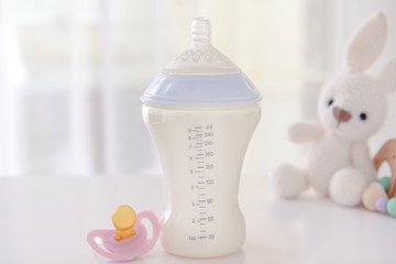 Bottle of milk for baby with pacifier on table indoors