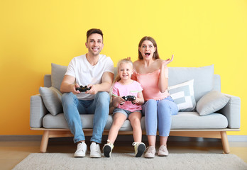 Young family playing video games while sitting on sofa near color wall