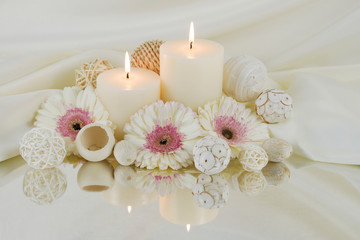 Spa concept of white burning candles with white Gerber flowers and natural potpourri elements reflecting in a mirror. Still life of white candles and flowers