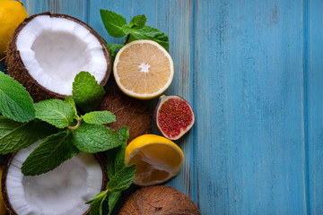 Chopped coconut halves with lemon and mint leaves on a blue wooden background. Tropical exotic background with coconut citruses and place for copy space. View from above