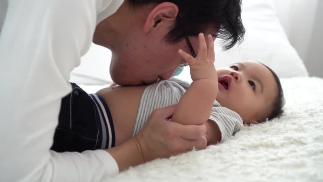 Family of young Asian father tenderly kissing his baby boy on his stomach with his wife. Man and woman enjoying their time with child