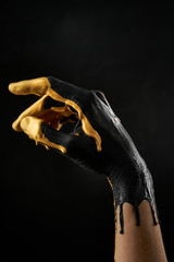 Female refined hand smeared with black and gold acrylic paint on a black background
