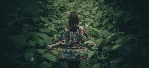 Woman in a colorful gown posing in a lush green jungle like forest or bush. Leaves surrounding a cute redhead girl exposing her colorful dress. - Powered by Adobe
