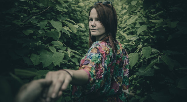 Young woman holding a man's hand and leading him into the wild green jungle like bush. Mystical photo of a girl leading  a man into the unknown.