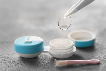 Taking of contact lens from case on grey background, closeup