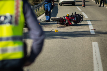 Car and a red sport motorcycle crash scene on an open road in afternoon. Workers and police seen...