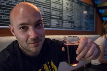 A young man is holding a glass of wine mixed with cola in his hands in a bar and encouraging to drink. Man drinking in a bar.