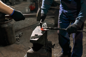 blacksmith with striker forges a horseshoe, close-up