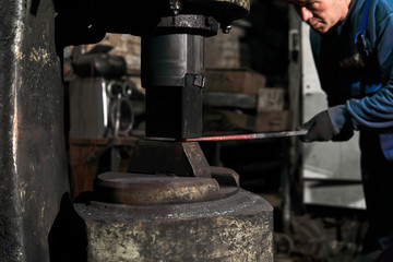 blacksmith processes a hot workpiece with a power hammer