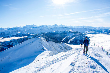Fototapeta na wymiar mountaineer at the summit against blue snow covered mountain layers. panoramic picture at the summit of the snowy mountain. panoramic winter landscape, sunny blue sky