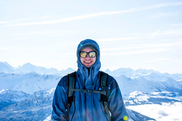 Fototapeta na wymiar mountaineer backpacker smiling at the summit against blue snowy mountain layers in winter. sunny, blue sky