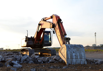 Excavator with a large iron bucket breaks asphalt on a construction site. Demolition work concrete,...