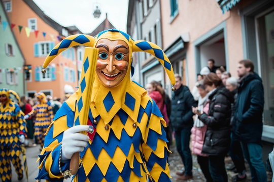 Bajass aus Waldkirch - Narrenfigur in gelb-blauem Gewand zeigt ein traditionälen Gegenstand, bei Fastnachtumzug in Staufen, Süd-Deutschland