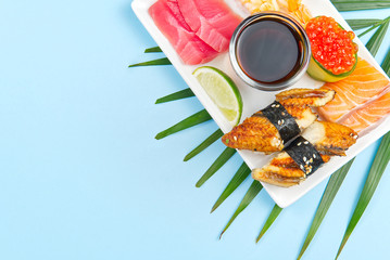 traditional japanese sushi set on a white plate isolated on a blue background. tasty set of sushi, nigiri, sahimi and maki. delicious dinner or lunch for one person. flat lay