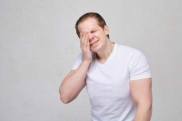 A man with a white T-shirt rubs his eyes in pain. Human vision problems. close up.