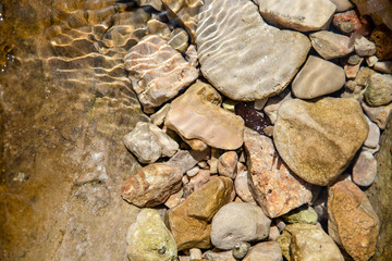 Stones in clear water, sun reflection, summertime. Natural background, top view, close up