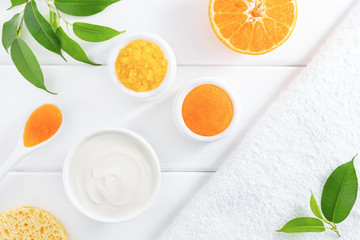 Natural homemade cosmetics: scrub, cream and sea salt with orange fruit on white background. Organic beauty or SPA concept. Flat lay, top view.