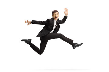 Cheerful young man in a black suit jumping and looking at camera