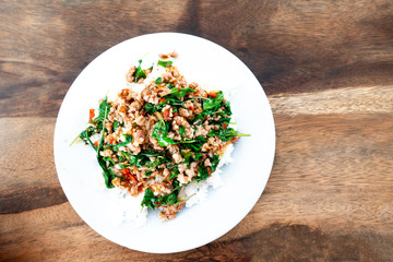 Rice topped with stir-fried pork and basil in a white dish.