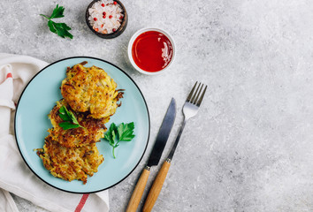 Homemade potato pancakes or hash brown on blue plate with sauce on gray table. Traditional dish in European and American cuisine. Top view.
